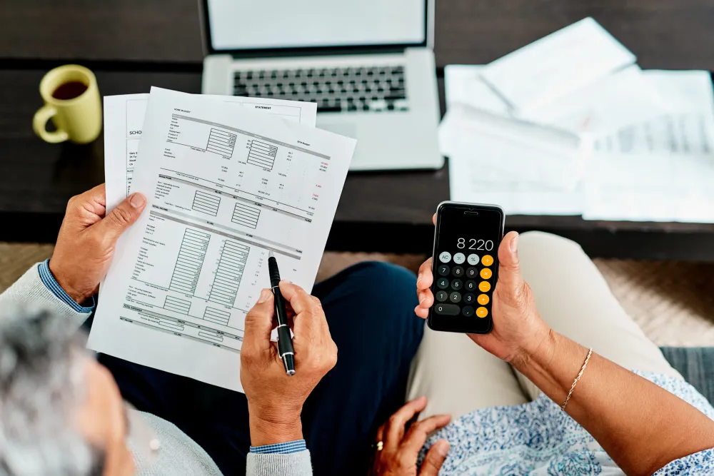 Reviewing financial statements with a calculator on a phone and a laptop nearby