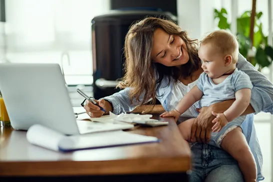 Parent working on taxes at a laptop with a baby on their lap
